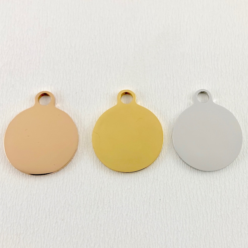 May include: Three round metal tags with a loop at the top. The tags are in rose gold, gold, and silver.