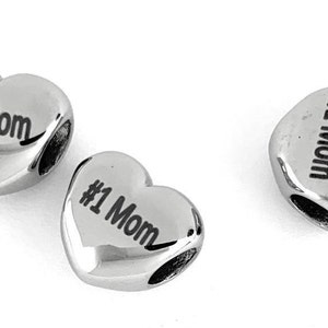 May include: Three silver heart-shaped charms with the text "#1 Mom" engraved on each.