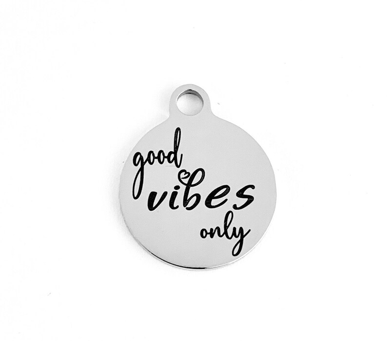 May include: Silver charm with the text "good vibes only" in black lettering.