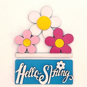 May include: Wooden sign with the text "Hello Spring" in white script on a blue background. Three wooden flowers are above the sign, one white with a yellow center, one pink with a yellow center, and one red with a yellow center.