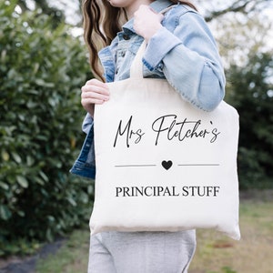 Könnte beinhalten: Eine weiße Stofftasche mit schwarzem Text, der "Mrs. Fletcher's" mit einem kleinen schwarzen Herzen und den Worten "PRINCIPAL STUFF" darunter lautet.