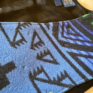 Puede incluir: Primer plano de un textil estampado en azul, negro y verde. El dise&ntilde;o presenta formas y l&iacute;neas geom&eacute;tricas. El textil es probablemente lana, con una etiqueta que dice "Pendleton" y "Made in USA."