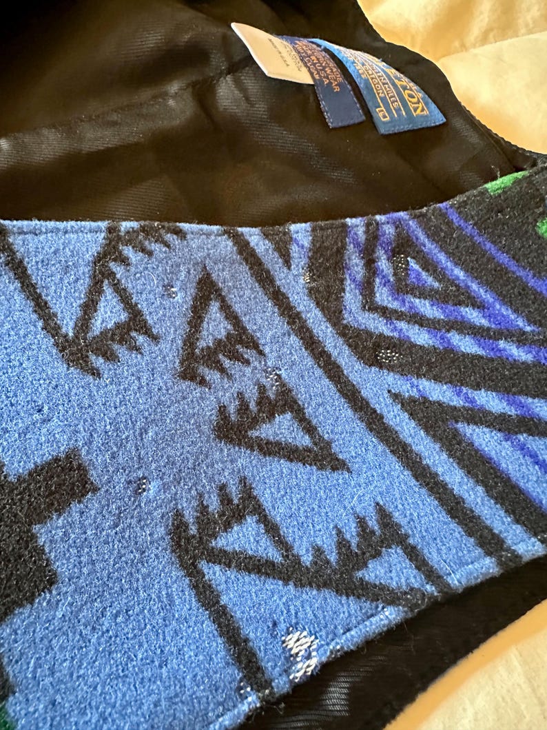 Puede incluir: Primer plano de un textil estampado en azul, negro y verde. El dise&ntilde;o presenta formas y l&iacute;neas geom&eacute;tricas. El textil es probablemente lana, con una etiqueta que dice "Pendleton" y "Made in USA."