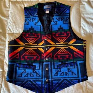 Può includere: Un gilet fantasia con scollo a V e chiusura con bottoni. Il design presenta forme geometriche in blu, rosso, giallo e verde. Il gilet ha due tasche anteriori e una fodera nera. Il marchio "Pendleton" è visibile su un'etichetta.