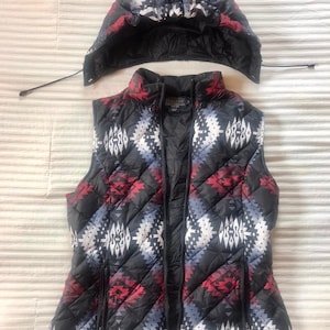 May include: A black quilted vest with a geometric pattern in red, white, and blue. The vest has a zipper closure and two pockets on the sides. The vest is made by Pendleton.