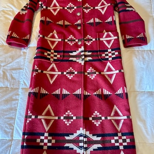 May include: A long, red coat with a geometric pattern in white, black, and brown. The coat has a black collar, two pockets, and silver buttons. The design features diamond and square shapes.