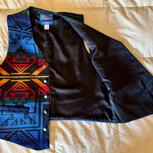 Puede incluir: Un chaleco estampado con interior negro. El chaleco presenta un dise&ntilde;o geom&eacute;trico en tonos de azul, rojo, amarillo y verde. Tiene cierre de botones y un peque&ntilde;o bolsillo. El chaleco est&aacute; abierto, mostrando el forro negro.