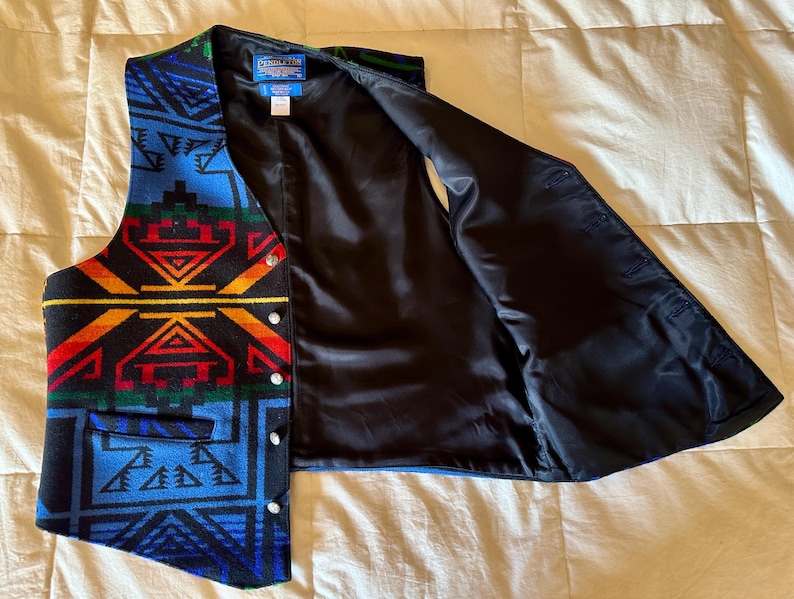 Puede incluir: Un chaleco estampado con interior negro. El chaleco presenta un dise&ntilde;o geom&eacute;trico en tonos de azul, rojo, amarillo y verde. Tiene cierre de botones y un peque&ntilde;o bolsillo. El chaleco est&aacute; abierto, mostrando el forro negro.