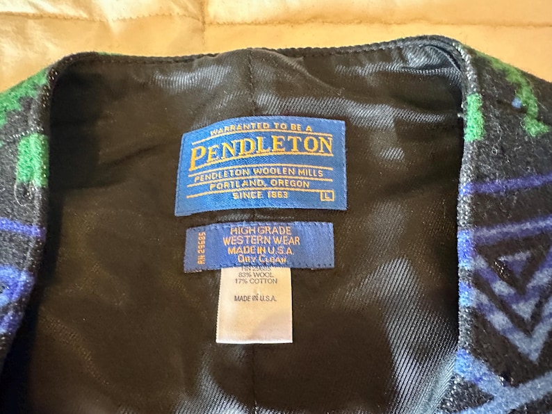 Puede incluir: Primer plano de un chaleco con estampado negro, azul y verde. El forro interior es negro. El chaleco tiene una etiqueta Pendleton con el texto "Pendleton Woolen Mills, Portland, Oregon, Since 1863". El chaleco est&aacute; hecho en los EE. UU.