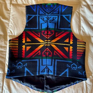 Puede incluir: Un chaleco negro con un vibrante patr&oacute;n geom&eacute;trico en azul, rojo, naranja, amarillo y verde. El chaleco tiene un forro negro y un dise&ntilde;o de cuello en V. El patr&oacute;n presenta formas angulares y dise&ntilde;os sim&eacute;tricos.