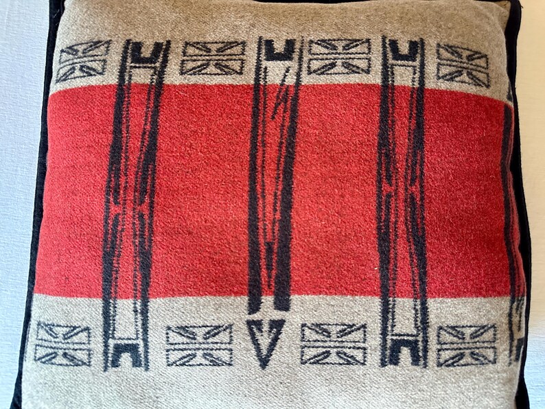 Peut inclure: Coussin carr&eacute; avec une bande centrale rouge et des bordures beiges. Le motif pr&eacute;sente des lignes verticales noires et des symboles Union Jack. Le coussin a une bordure noire.