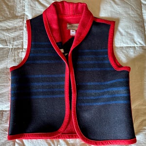 May include: A wool vest with a red collar and trim. The vest is primarily navy blue with horizontal blue stripes. The interior and trim are red. The vest has a label that reads "Pendleton Originals".