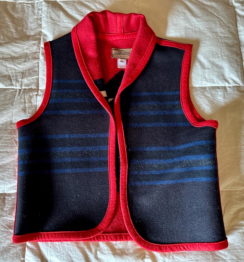 May include: A wool vest with a red collar and trim. The vest is primarily navy blue with horizontal blue stripes. The interior and trim are red. The vest has a label that reads "Pendleton Originals".