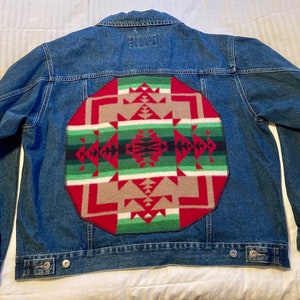 May include: A blue denim jacket with a large red, green and brown patterned patch on the back.