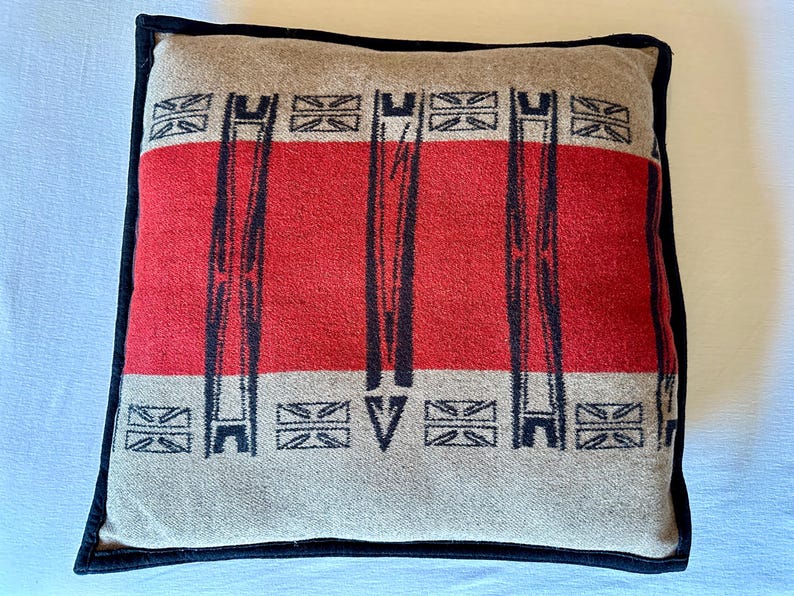 Peut inclure: Coussin carr&eacute; avec un motif beige et rouge. Le coussin pr&eacute;sente une bande rouge centrale avec des lignes verticales noires et des formes g&eacute;om&eacute;triques. Il est bord&eacute; d'une bordure noire.