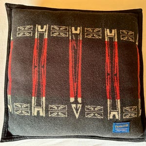 Peut inclure: Un coussin carr&eacute; avec un fond gris fonc&eacute; et une bordure noire. Le coussin pr&eacute;sente un motif de rayures verticales rouges et de formes g&eacute;om&eacute;triques blanches et grises. Une &eacute;tiquette bleue avec du texte blanc est visible en bas &agrave; droite.