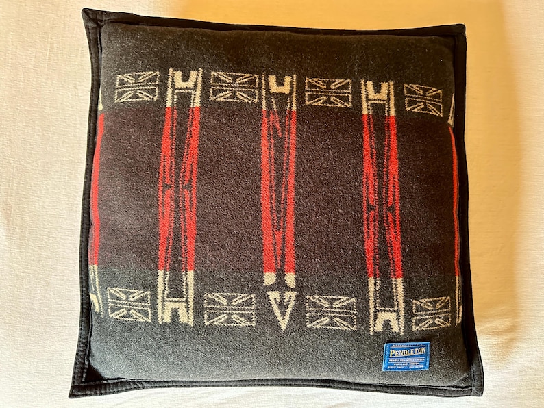 Peut inclure: Un coussin carr&eacute; avec un fond gris fonc&eacute; et une bordure noire. Le coussin pr&eacute;sente un motif de rayures verticales rouges et de formes g&eacute;om&eacute;triques blanches et grises. Une &eacute;tiquette bleue avec du texte blanc est visible en bas &agrave; droite.