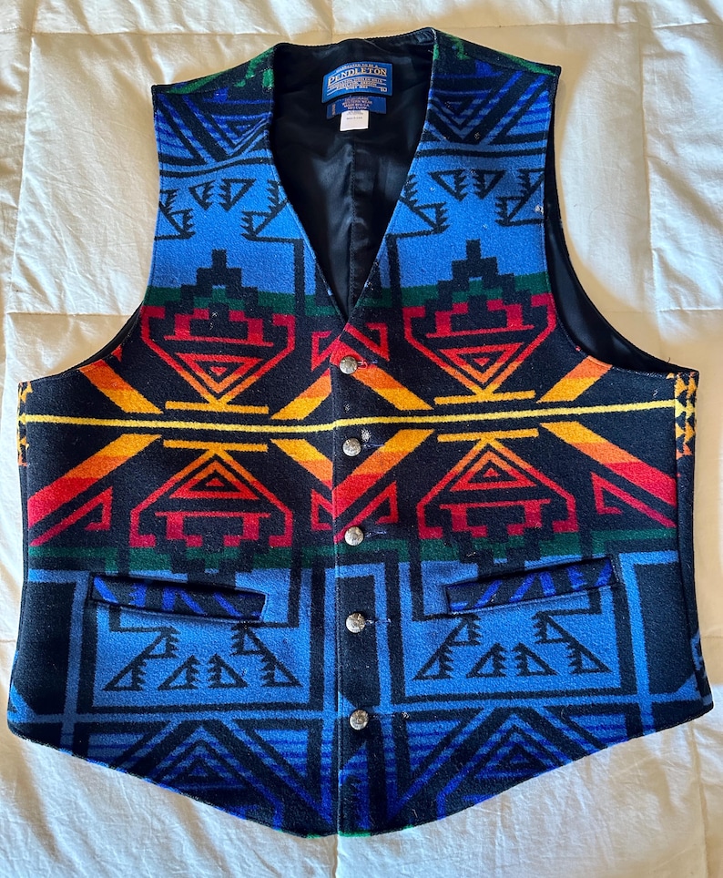 Puede incluir: Un chaleco colorido con un patr&oacute;n geom&eacute;trico en azul, negro, rojo, amarillo y verde. El chaleco tiene cuello en V, cuatro botones plateados y dos bolsillos delanteros. El interior es negro.