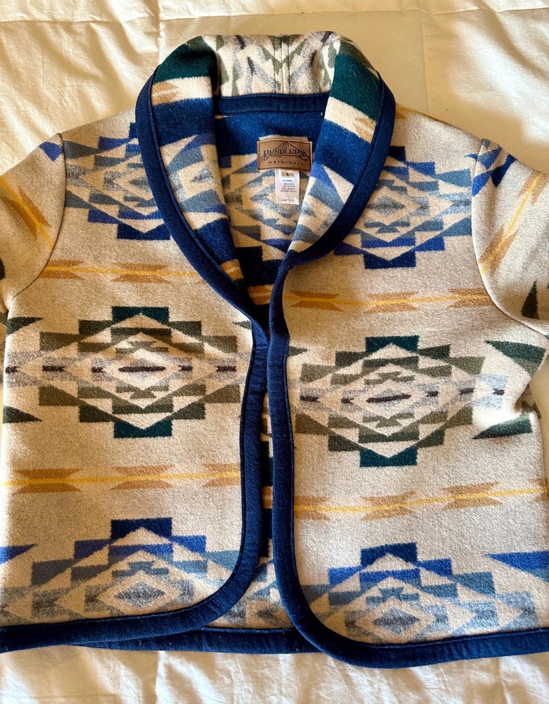 Może przedstawiać: Beżowa wełniana kurtka z geometrycznym wzorem w kolorze niebieskim, zielonym i ż&oacute;łtym. Kurtka ma granatowe wykończenie i kołnierz. Etykieta Pendleton jest widoczna z przodu.