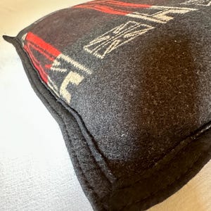 Peut inclure: Un coussin gris fonc&eacute; avec un motif g&eacute;om&eacute;trique rouge et blanc. Le coussin a une bordure noire et est fait d'un tissu textur&eacute;. Le motif comprend des formes blanches et des rayures rouges.