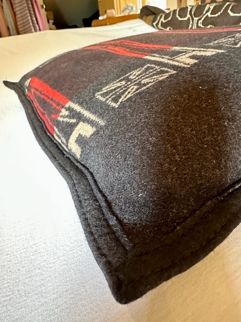 Peut inclure: Un coussin gris fonc&eacute; avec un motif g&eacute;om&eacute;trique rouge et blanc. Le coussin a une bordure noire et est fait d'un tissu textur&eacute;. Le motif comprend des formes blanches et des rayures rouges.