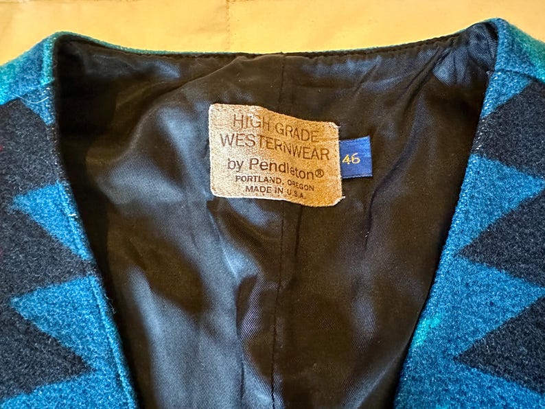 May include: Close-up of a turquoise and black patterned vest with a black lining. The vest has a tag that reads "HIGH GRADE WESTERNWEAR by Pendleton Portland, Oregon MADE IN U.S.A." A blue tag with the number "46" is also visible.