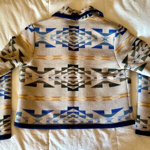 Może przedstawiać: Beżowa kurtka z geometrycznym wzorem w kolorze niebieskim, zielonym i ż&oacute;łtym. Kurtka ma granatowy kołnierz i wykończenia. Wz&oacute;r powtarza się na plecach i rękawach.