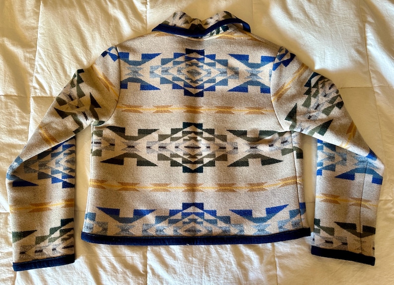 Może przedstawiać: Beżowa kurtka z geometrycznym wzorem w kolorze niebieskim, zielonym i ż&oacute;łtym. Kurtka ma granatowy kołnierz i wykończenia. Wz&oacute;r powtarza się na plecach i rękawach.