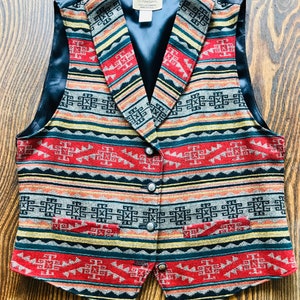 May include: A black and brown patterned vest with a black satin lining and silver buttons. The vest has a southwestern design with geometric shapes and stripes in red, yellow, and blue.