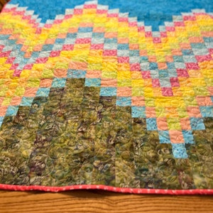 May include: A colorful quilt with a patchwork design featuring a green, brown, and yellow pattern. The quilt is made with squares of different colors, including pink, blue, yellow, and green. The quilt is quilted with a circular pattern.