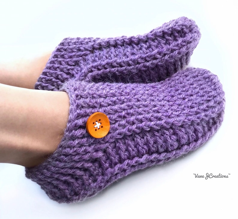 Op de afbeelding: Paarse gebreide pantoffels met een houten knoop. De sokken zijn zacht en comfortabel, perfect om je voeten warm te houden in de winter.