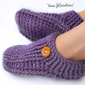 Op de afbeelding: Paarse gebreide pantoffels met een houten knoop. De pantoffels hebben een kabelbreipatroon.