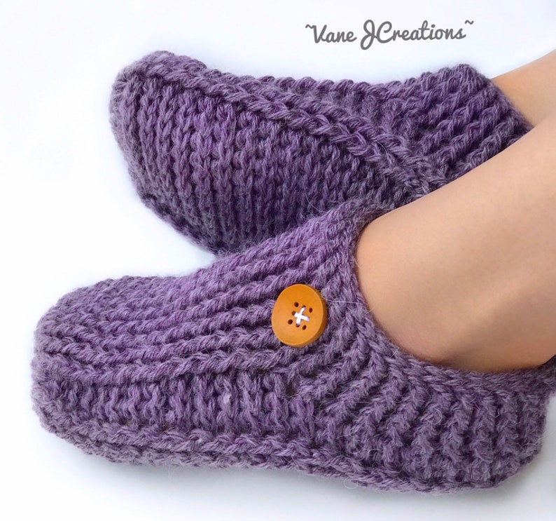 Op de afbeelding: Paarse gebreide pantoffels met een houten knoop. De pantoffels hebben een kabelbreipatroon.
