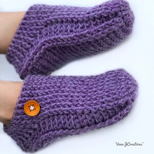 Op de afbeelding: Paarse gebreide pantoffels met een knoop op &eacute;&eacute;n pantoffel. De pantoffels zijn gemaakt met een eenvoudig steekpatroon.