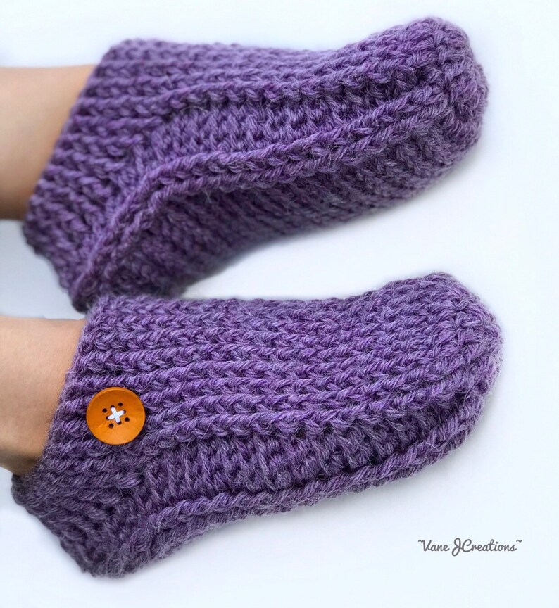 Op de afbeelding: Paarse gebreide pantoffels met een knoop op &eacute;&eacute;n pantoffel. De pantoffels zijn gemaakt met een eenvoudig steekpatroon.