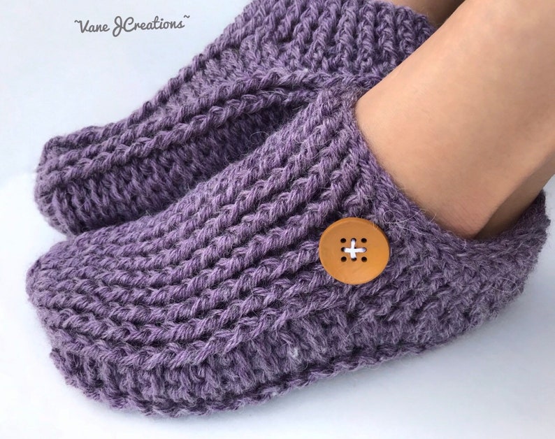 Op de afbeelding: Paarse gebreide pantoffels met een houten knoop aan de bovenkant. De pantoffels zijn zacht en comfortabel, perfect om je voeten warm te houden in de winter.