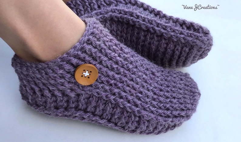 Op de afbeelding: Paarse gebreide pantoffels met een houten knoop op &eacute;&eacute;n sok.  "Vane J Creations" staat in de rechterbovenhoek van de afbeelding.