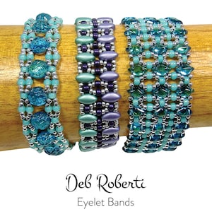Peut inclure: Trois bracelets en perles dans des tons de bleu, vert et violet. Les bracelets sont faits de petites perles rondes et sont disposés en un motif géométrique. Les bracelets sont présentés sur une surface en bois. Le texte "Deb Roberti Eyelet Bands" est affiché sous les bracelets.