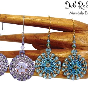 May include: Three pairs of beaded mandala earrings. The earrings are silver, gold, and silver with purple and blue beads. The earrings are on a wooden display stand. Deb Roberti Mandala Earrings.