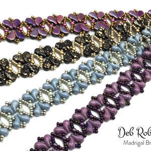 May include: Four beaded bracelets in different colors, including purple, black, blue, and light blue. The bracelets are made with small, teardrop-shaped beads and feature a repeating pattern. The bracelets are arranged in a stack, with the purple bracelet on top and the light blue bracelet on the bottom. The text "Deb Roberti Madrigal Bracelet" is visible at the bottom of the image.