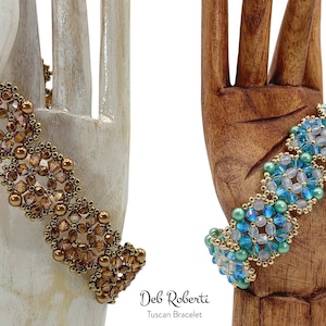 May include: Two beaded bracelets, one in gold and brown tones and the other in blue and green tones, are displayed on wooden hands. The bracelets are made with small beads and feature a floral design. The text "Deb Roberti Tuscan Bracelet" is displayed below the bracelets.