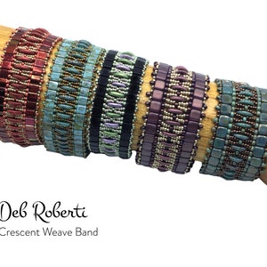 Pode incluir: Cinco pulseiras de contas em diferentes cores e padrões, incluindo vermelho, turquesa, roxo e verde. As pulseiras estão empilhadas em uma superfície de madeira e são etiquetadas como "Deb Roberti Crescent Weave Band".