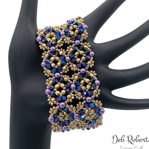 Puede incluir: Un brazalete de cuentas doradas y moradas con un patrón geométrico. El brazalete se llama "Tuscan Cuff" de Deb Roberti.