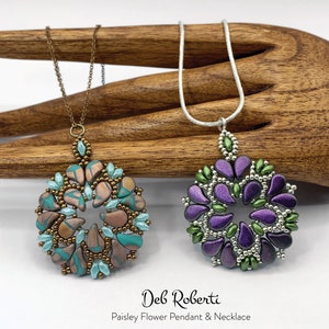 May include: Two beaded necklaces with paisley flower pendants. One pendant is brown, turquoise, and silver. The other pendant is purple, green, and silver. The necklaces are displayed on a wooden hand.