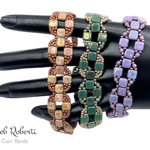 Op de afbeelding: Drie kralenarmbanden in een muntpatroon. De armbanden zijn in koper-, groen- en paarse tinten. De armbanden bevinden zich op een zwarte mannequinhand. De tekst "Deb Roberti Coin Bands" staat onder de armbanden.