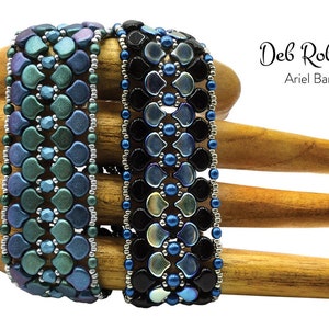May include: Two beaded bracelets on a wooden hand form. The bracelet on the left is blue, green, and silver. The bracelet on the right is black, blue, and silver. The bracelets are labeled "Deb Roberti Ariel Band".
