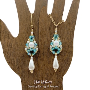 Puede incluir: Pendientes y colgante de gota de oro con cuentas azules y blancas. Los pendientes y el colgante tienen una perla blanca grande en el centro.