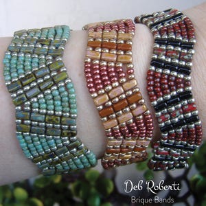 Könnte beinhalten: Drei Perlenarmbänder in einem wellenförmigen Muster. Die Armbänder sind aus türkisfarbenen, silbernen, braunen, orangefarbenen, rosafarbenen, roten und schwarzen Perlen gefertigt. Die Armbänder sind auf dem Handgelenk einer Person übereinander gelegt. Der Text "Deb Roberti Brique Bands" befindet sich am unteren Rand des Bildes.