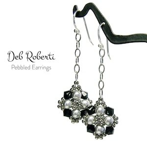 Può includere: Un paio di orecchini pendenti in argento con perline nere e bianche. Gli orecchini sono su un espositore. "Deb Roberti Pebbled Earrings" è scritto sotto gli orecchini.