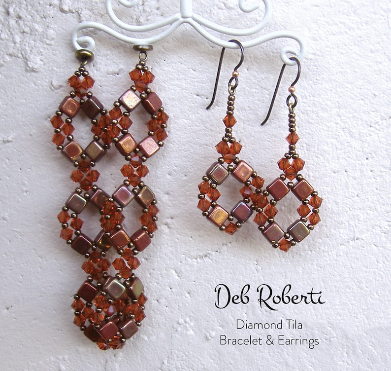 May include: A pair of long, brown and orange beaded earrings with a diamond shape design, and a pair of shorter earrings with the same design. The earrings are hanging on a white stand. The text "Deb Roberti" and "Diamond Tila Bracelet & Earrings" is below the earrings.